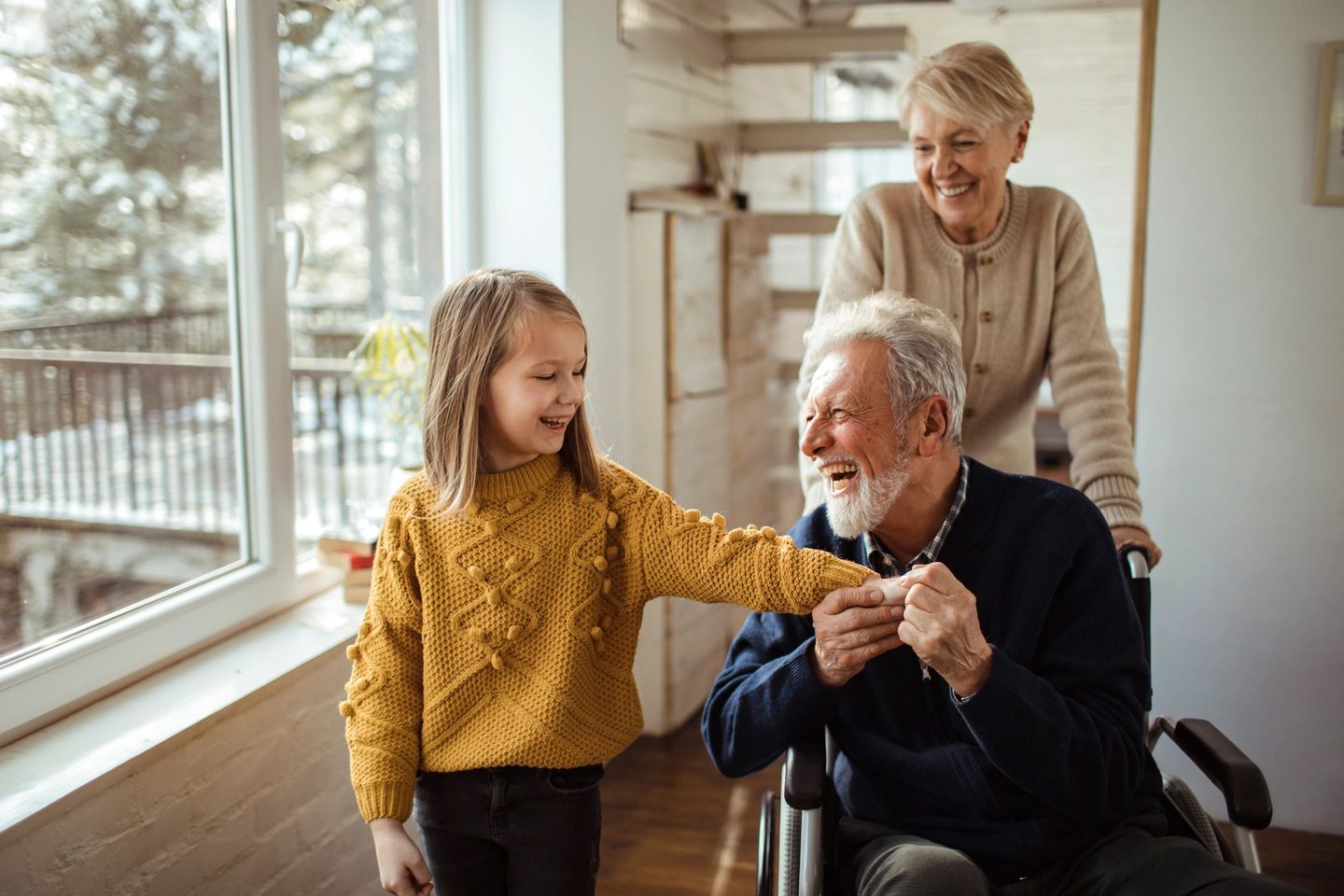 A grandchild and a caregiver sharing a moment with a smiling senior resident at home